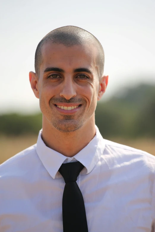 a man in white shirt and black tie smiling for the camera