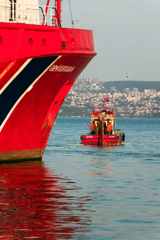 a red boat on the water near a large ship