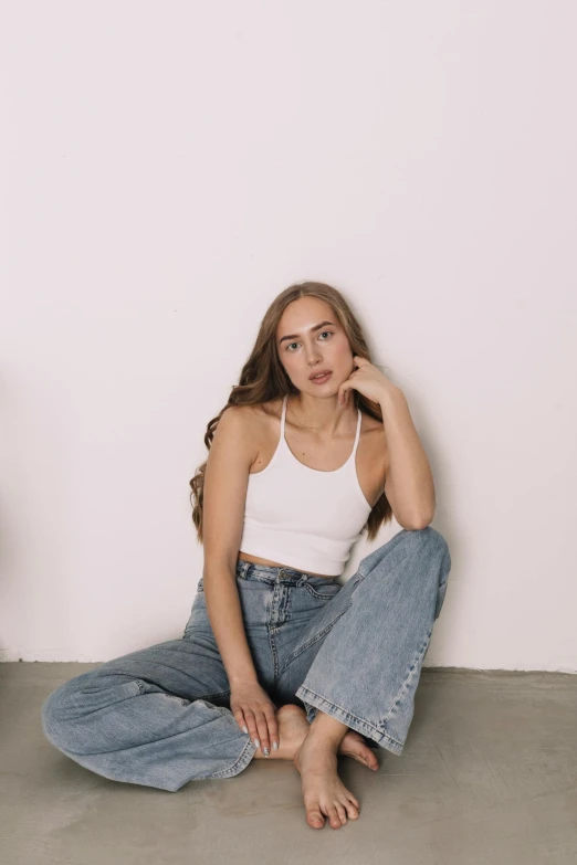 the  is posing for a po wearing denim pants and a white tank top