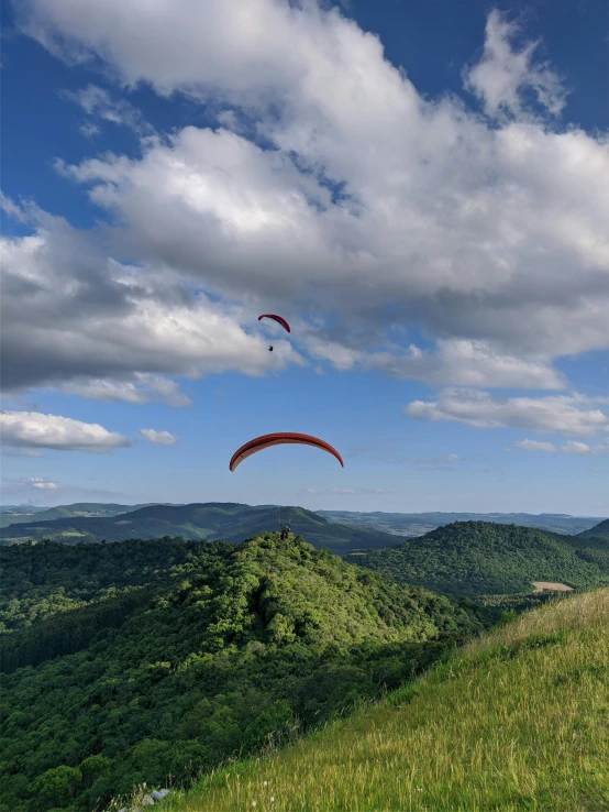 two people para sailing on top of a lush green hill