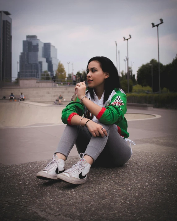 a woman wearing white tennis shoes, and green jacket eating a snack