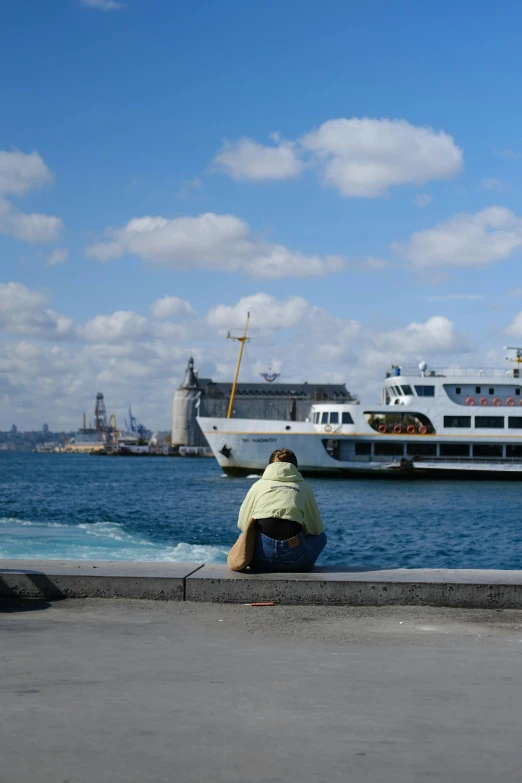 the man is sitting on the ledge next to the water watching the boat pass by