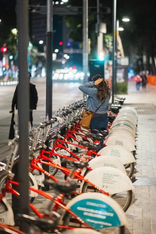 a woman sits at a street side long row of bicycles