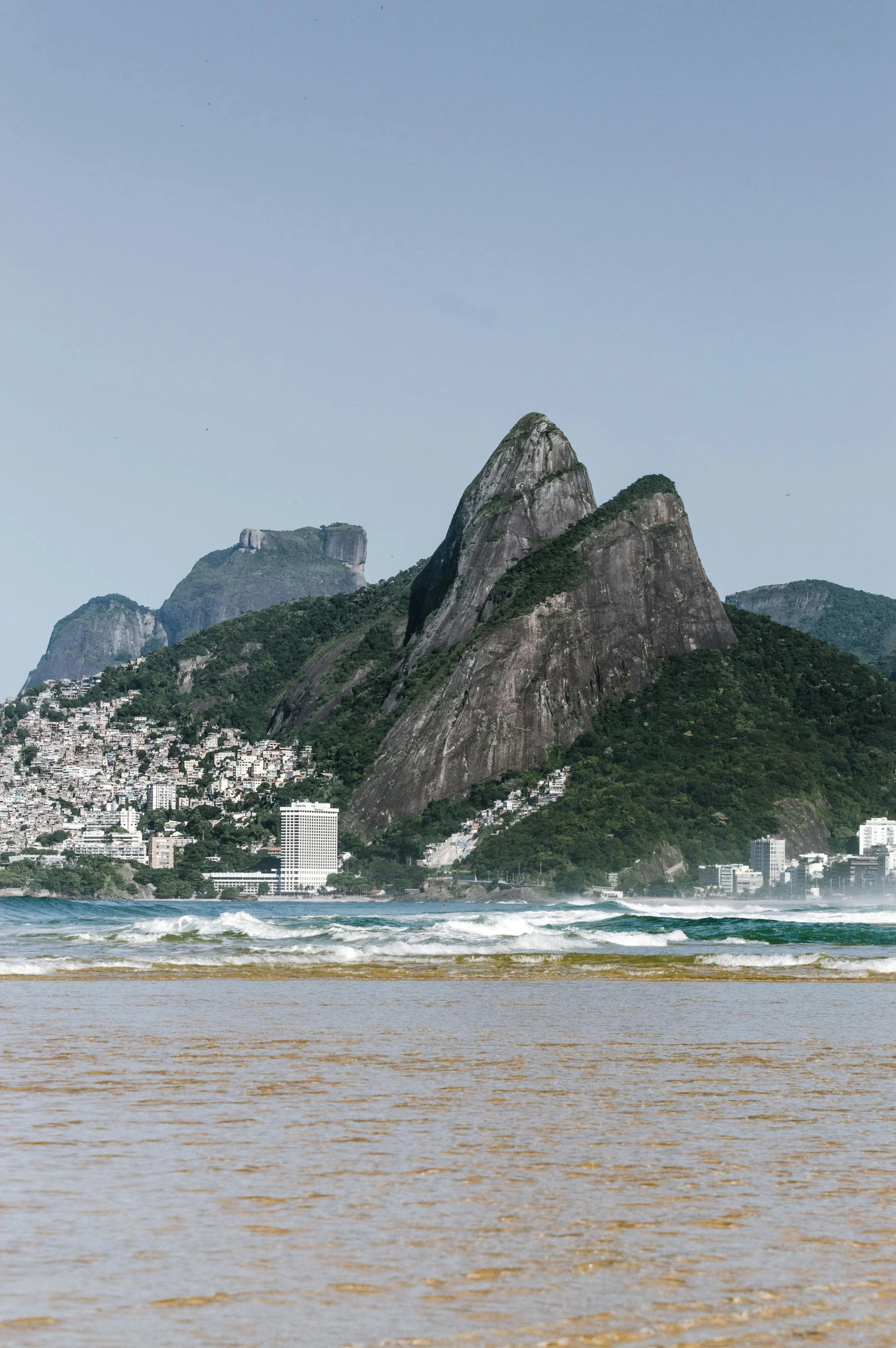 the mountains are behind the sea and there is a beach with surfers