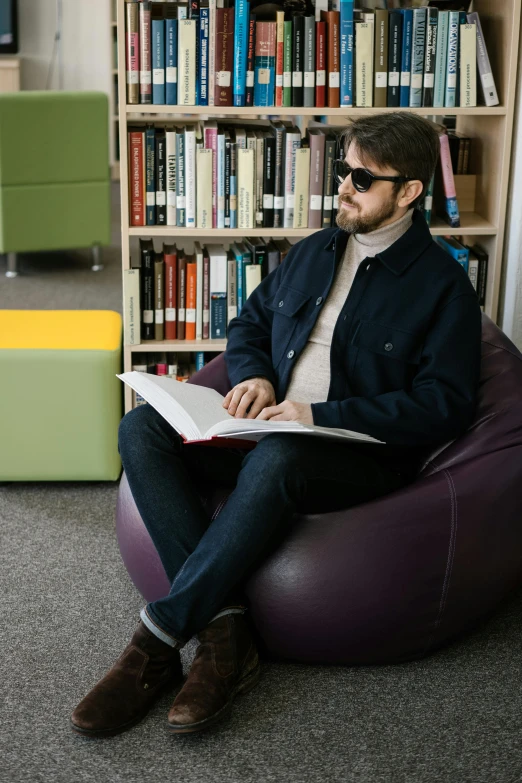 a man sitting on a bean bag chair in front of a book shelf