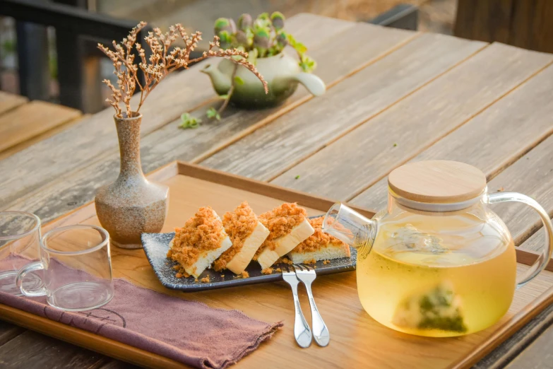 a wooden table with a tray and glassware, tea and a plate filled with food