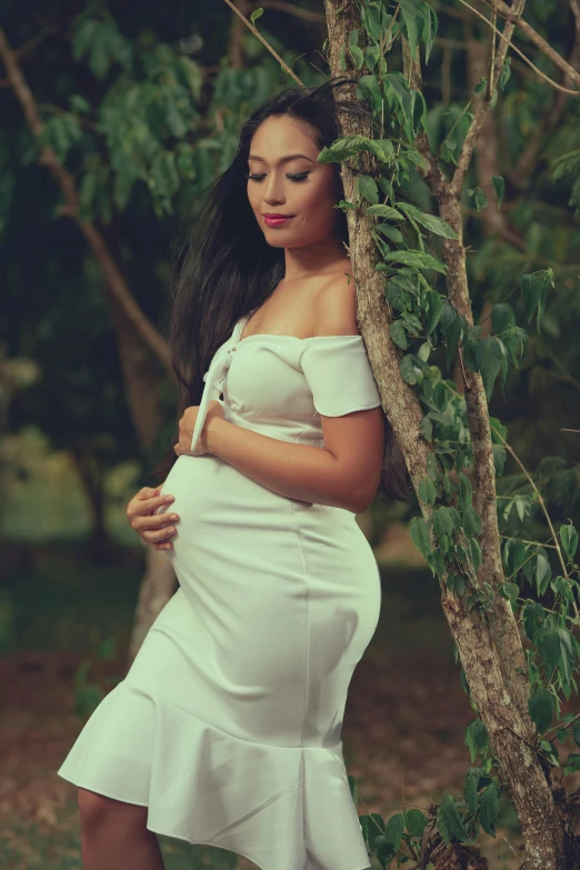 a pregnant woman in a dress leaning against a tree