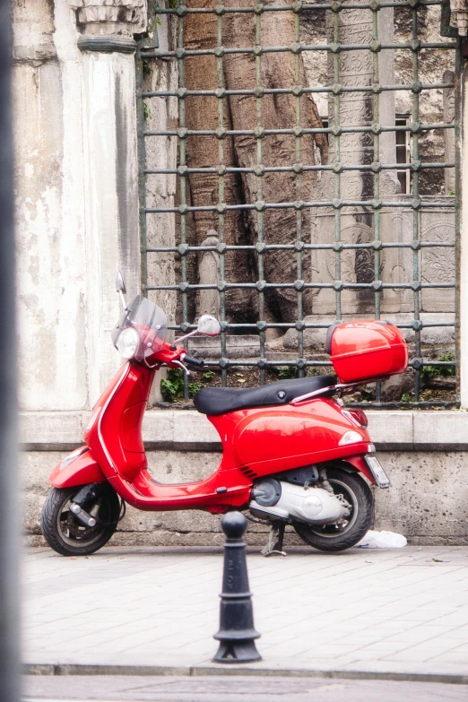 a red moped parked next to an old building with a chain link fence