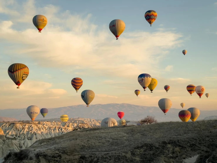 many balloons are flying over a hill on a sunny day