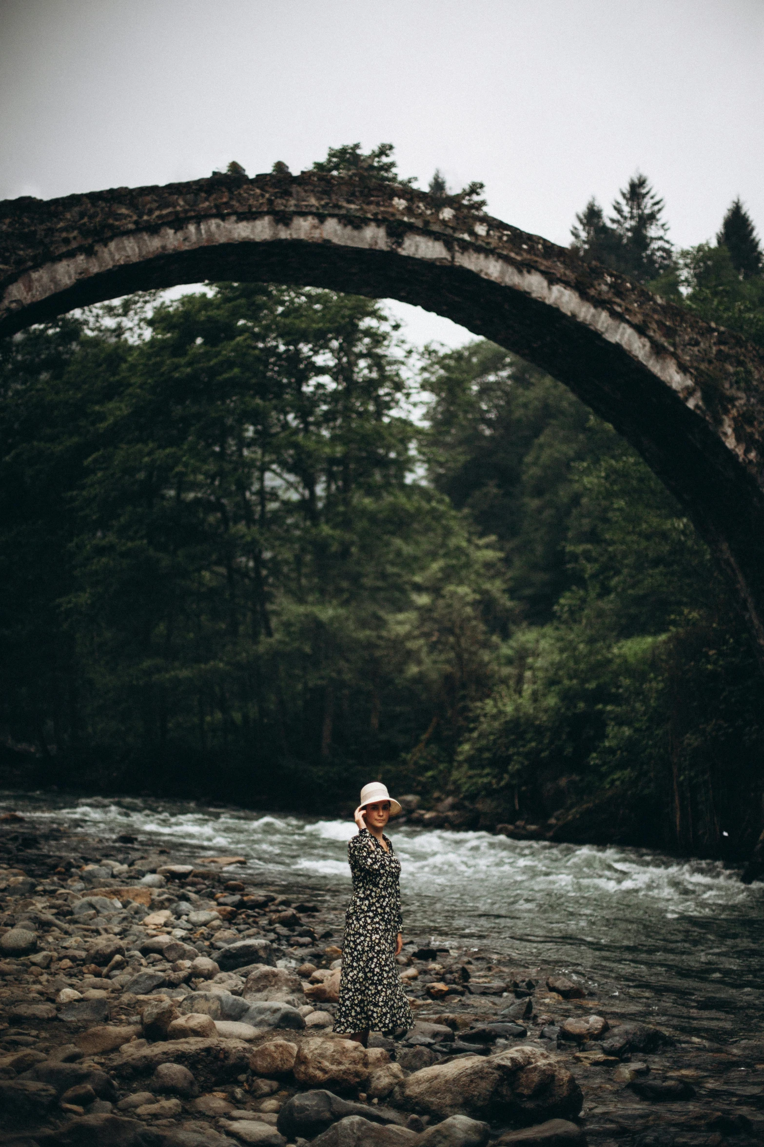 a person standing on rocks by water under a stone archway