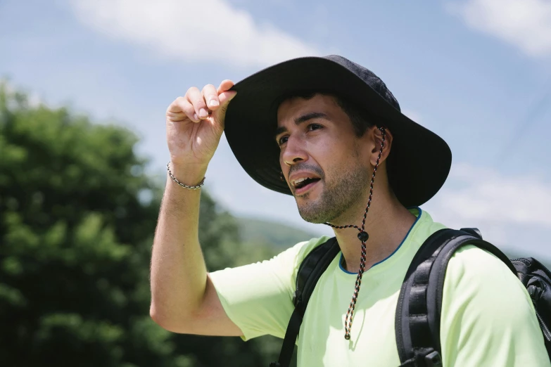 a man in a green shirt, black hat and back pack