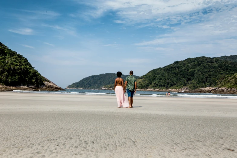 two people walking on the beach by the ocean