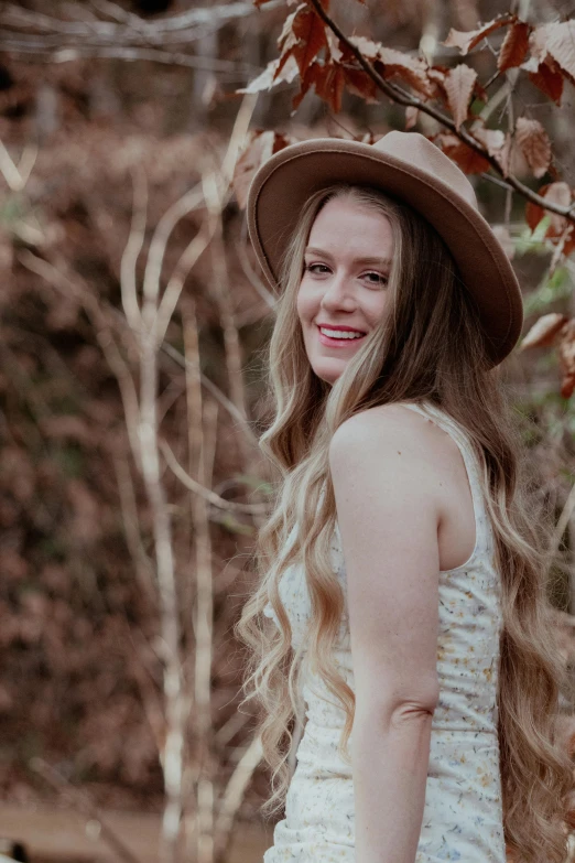 young woman in a hat smiling while standing in the woods