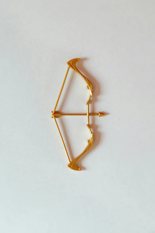 a gold plated arrow shaped brooch sitting on top of a white surface