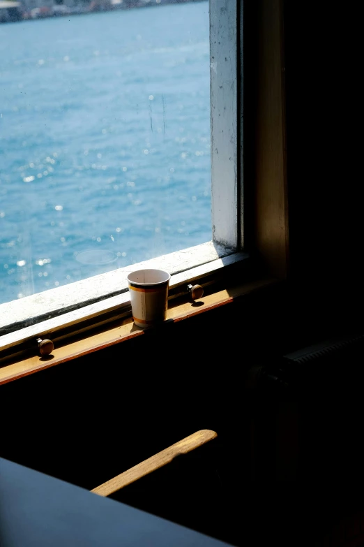 there is a cup on the window sill overlooking the water