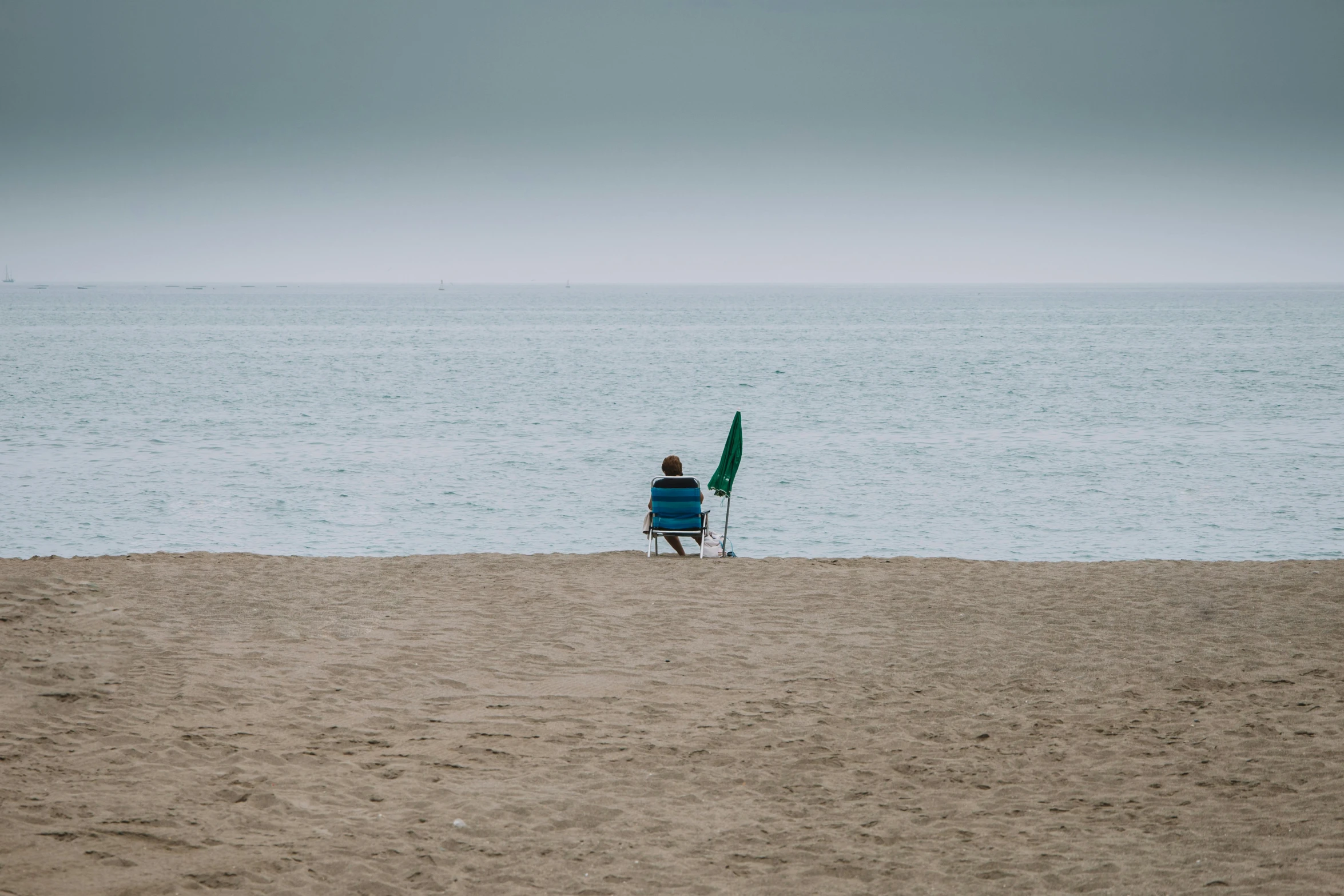 two people sitting at the beach on a bench holding an umbrella