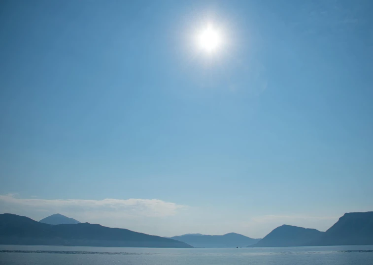 bright blue sky with some mountains and the sun in front