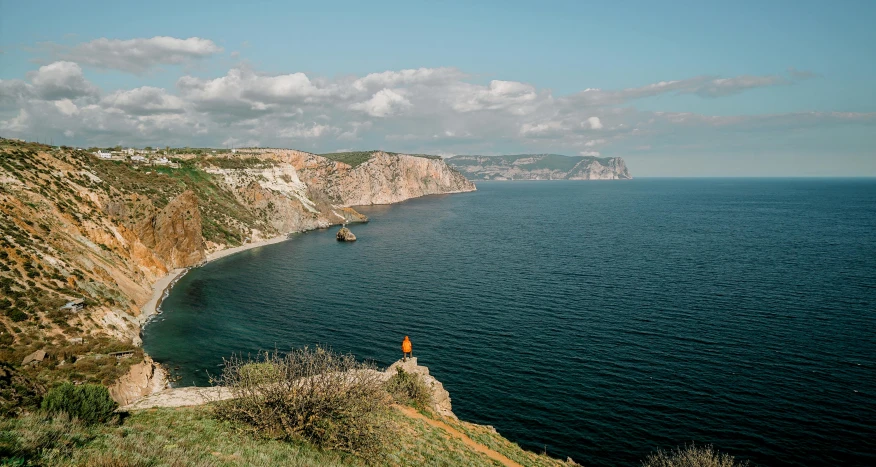 an ocean landscape with cliffs in the foreground and a lone orange cone in the distance