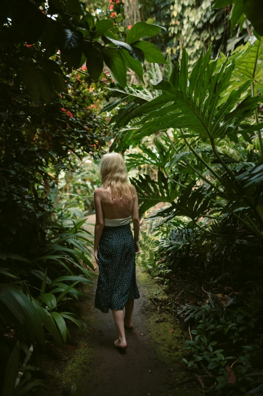 a woman walking down a path near some jungle plants