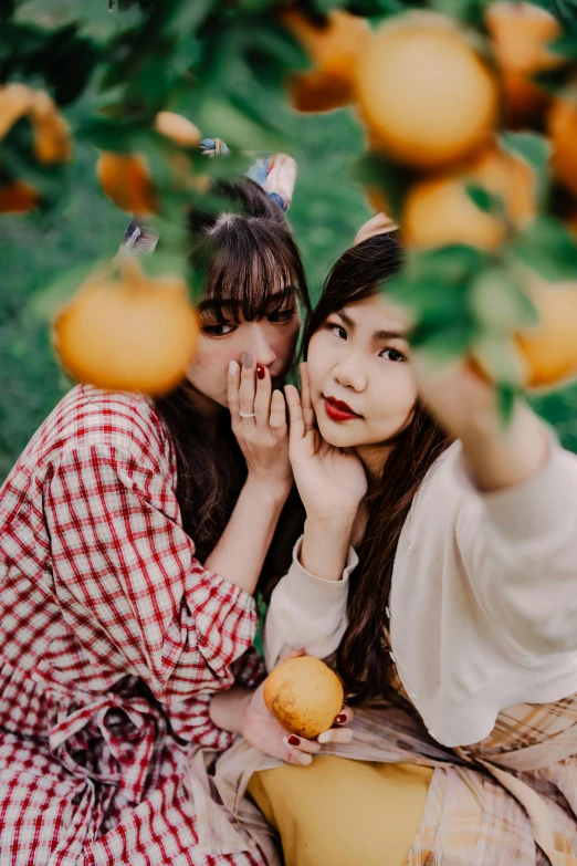 two beautiful young ladies sitting in front of fruit trees