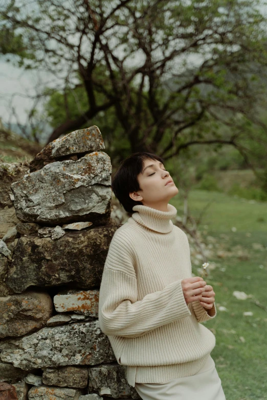 a woman in white sweater leaning on wall with flowers