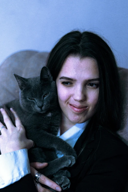 a woman holds a grey cat while wearing a suit jacket