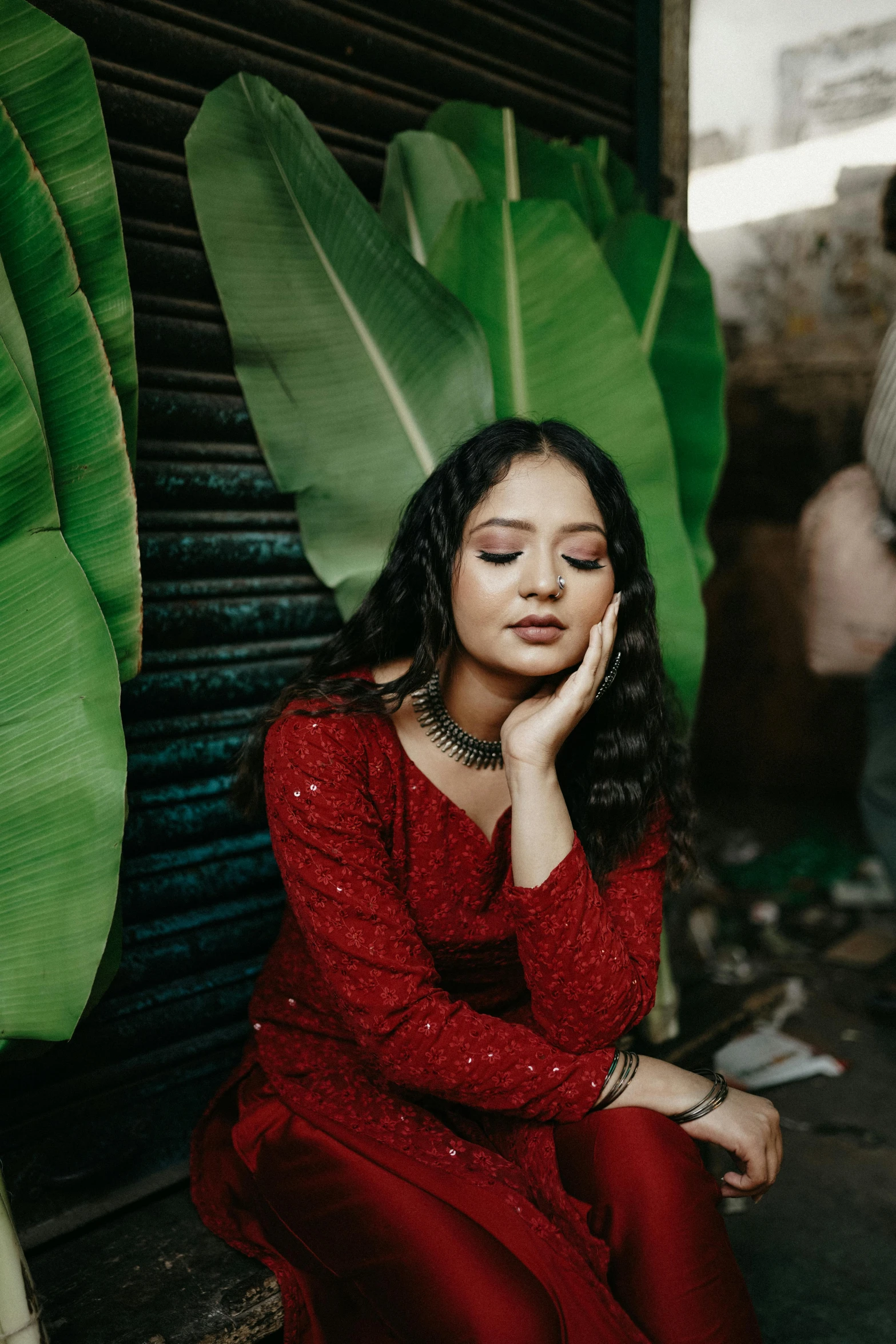 a young woman is sitting on the ground next to a plant