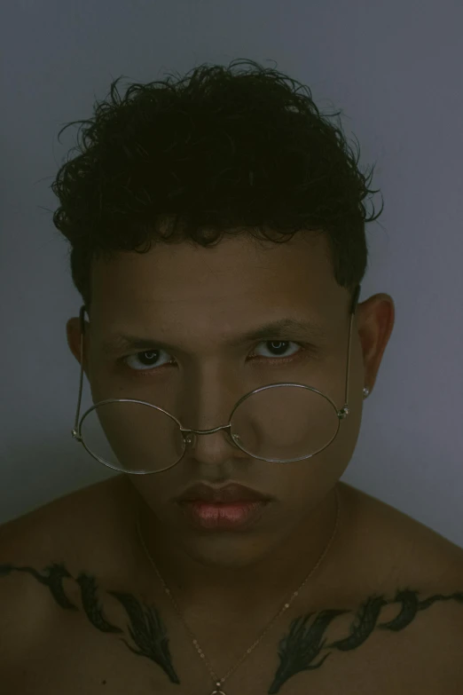 man with fake eyelashes standing shirtless in a darkened room