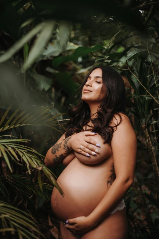 a pregnant woman with tattoo standing in the jungle