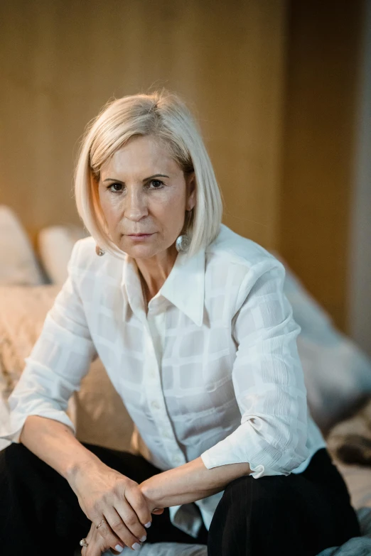 a blonde woman sitting on the bed looking serious