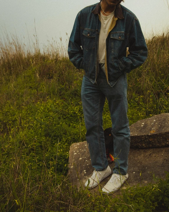 a man in jeans and a hat standing on a rock