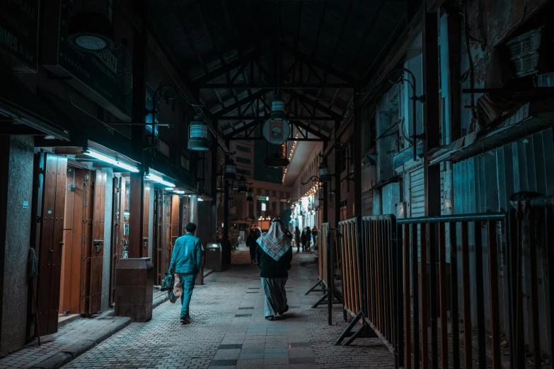 a dark street at night with people walking on the sidewalk and one person holding an umbrella