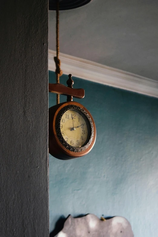 the clock is hanging from a wall with some rope