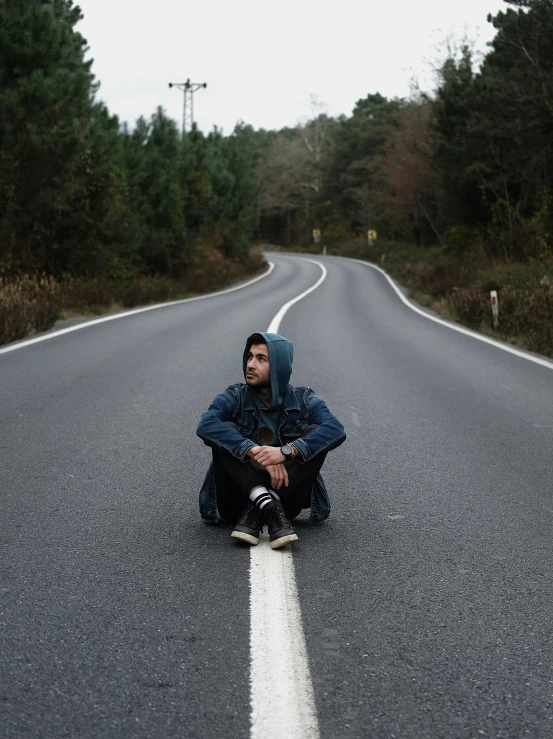 a man sitting on the side of a road looking down at his shoes