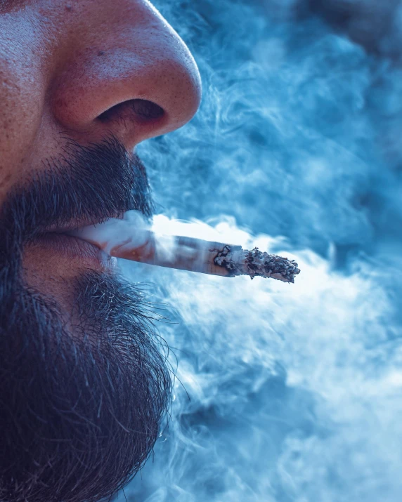 a man with a cigarette in his mouth and on the other hand looks up at the smoke from the cigarette