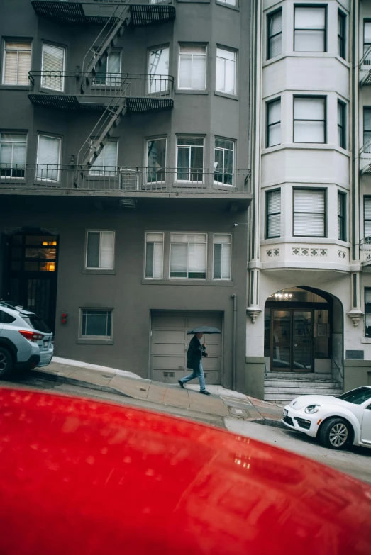 a person walking past a red parked car on the sidewalk