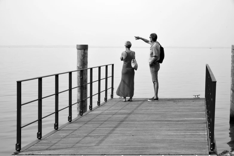 a man and woman standing on a pier pointing at the water