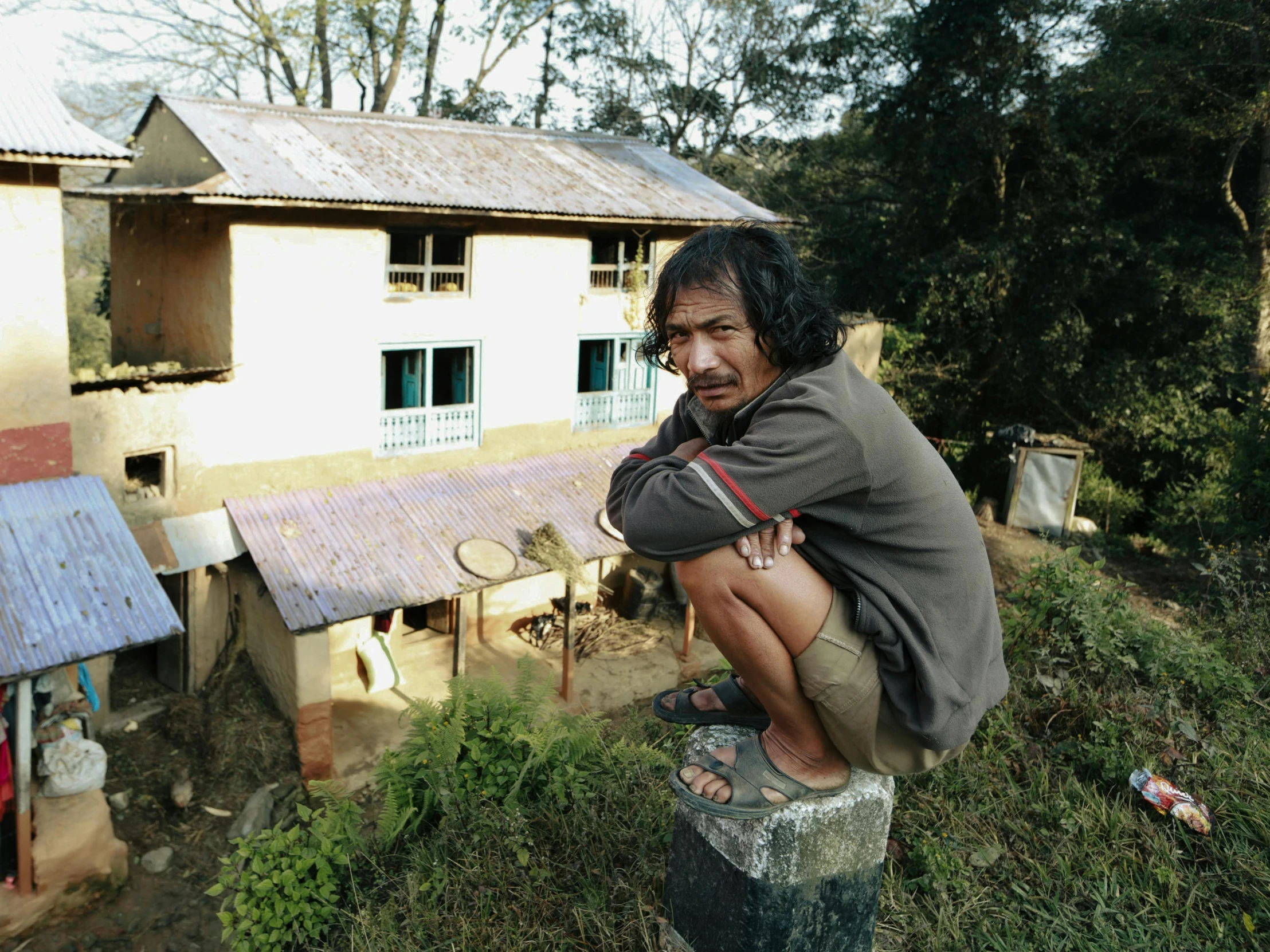 man posing on top of cement block with house in background