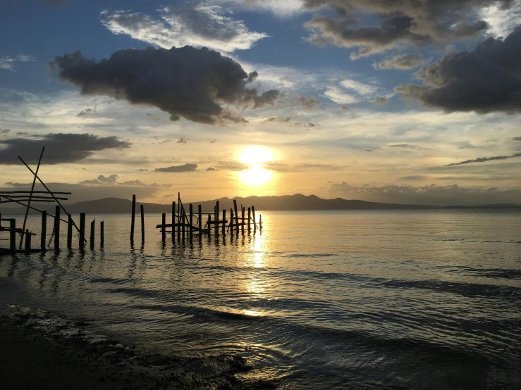 the sun sets over an ocean with old wooden posts in the water