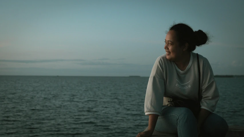 the girl is sitting on a ledge looking over the water