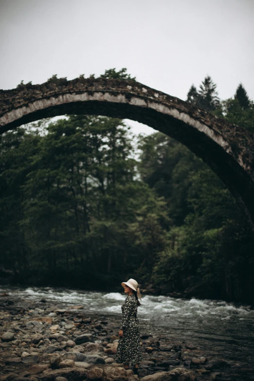 the woman is standing by the water wearing a hat