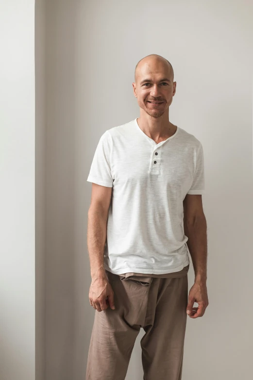 a bald man smiles in a white shirt and beige pants