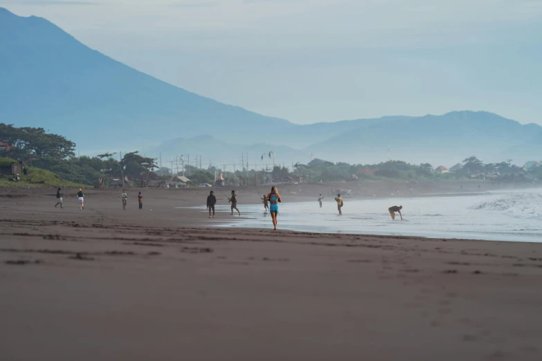 many people walk on the beach with the mountains in the background