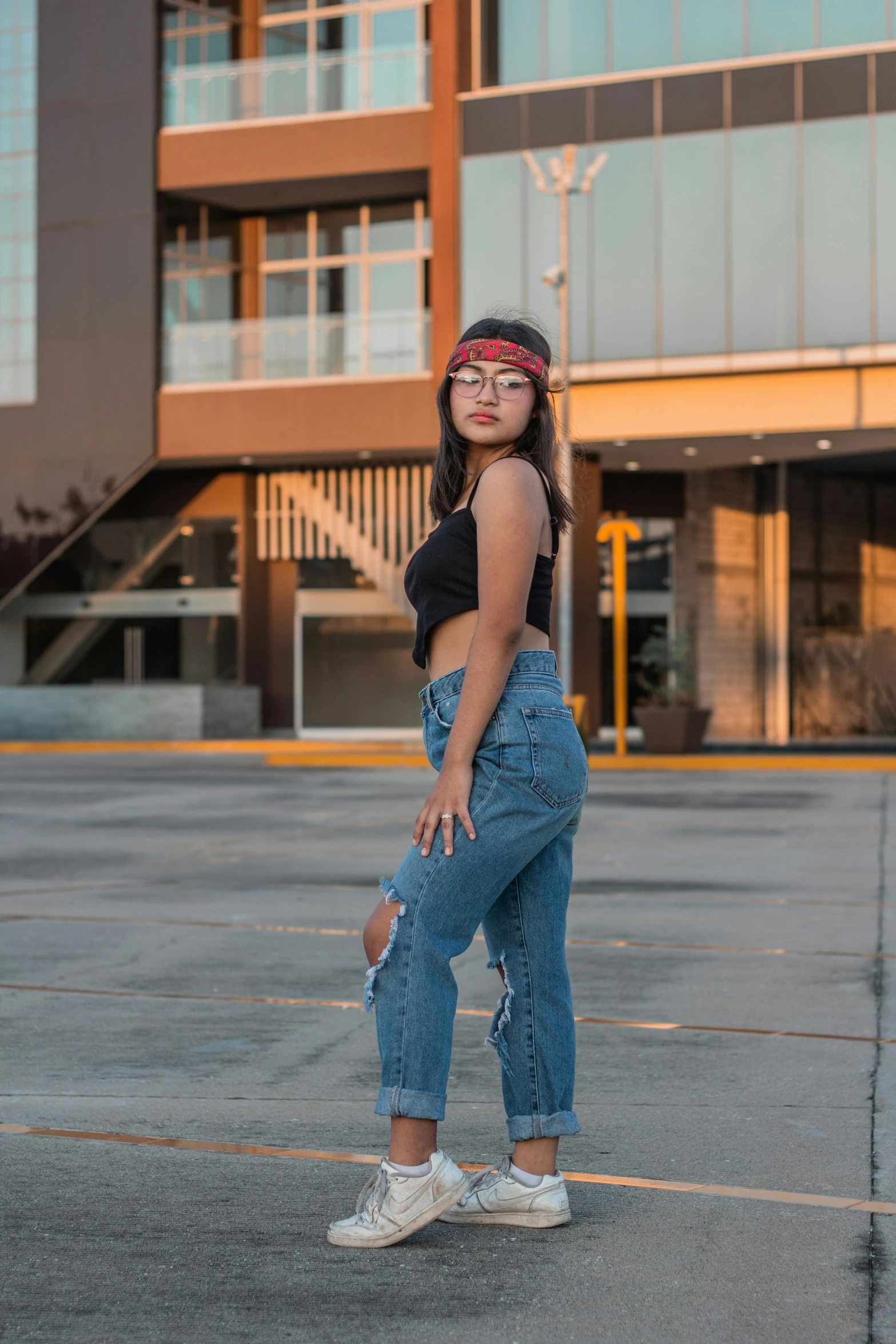 an asian girl in ripped jeans and a black tank top, stands against the building