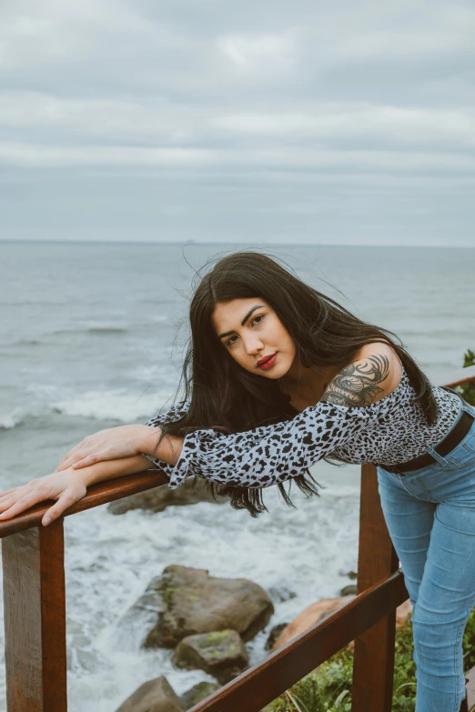 a woman with a tattoo leaning over a rail near the ocean