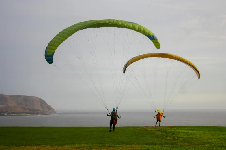 two people are walking on the grass while holding onto parachutes