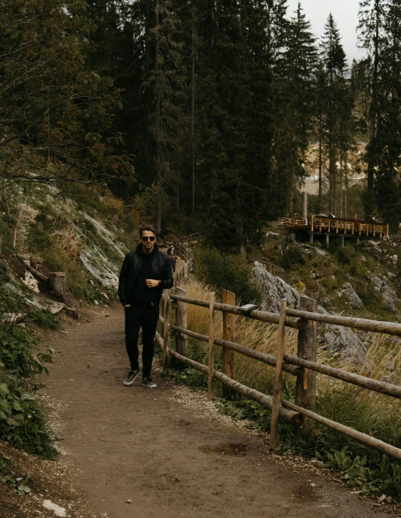 a man in a black jacket and a long wooden fence near some trees