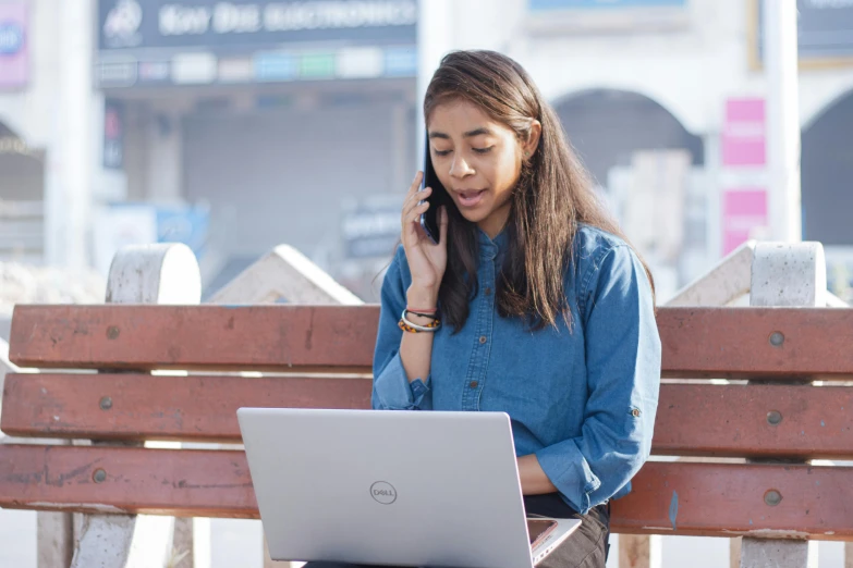 the woman on the bench is talking on the phone and looking at her laptop