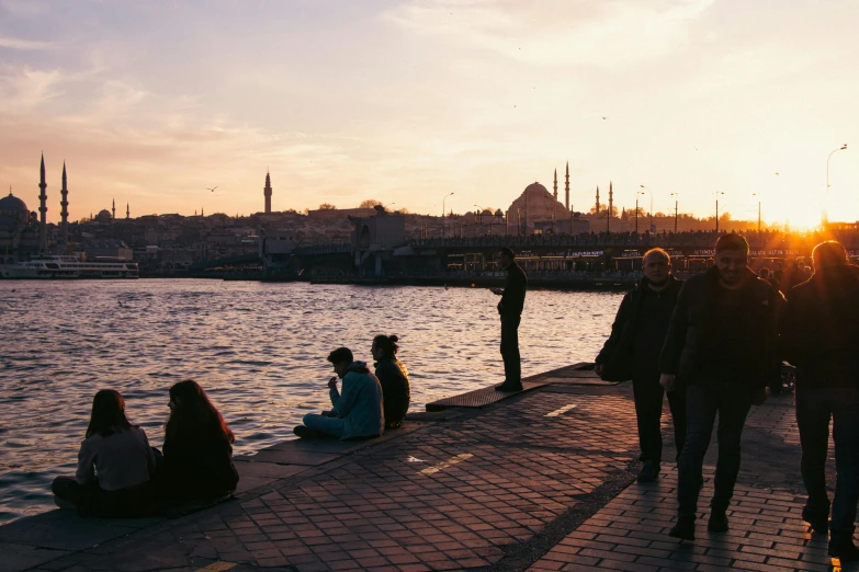 people sitting by the waters edge watching sunset