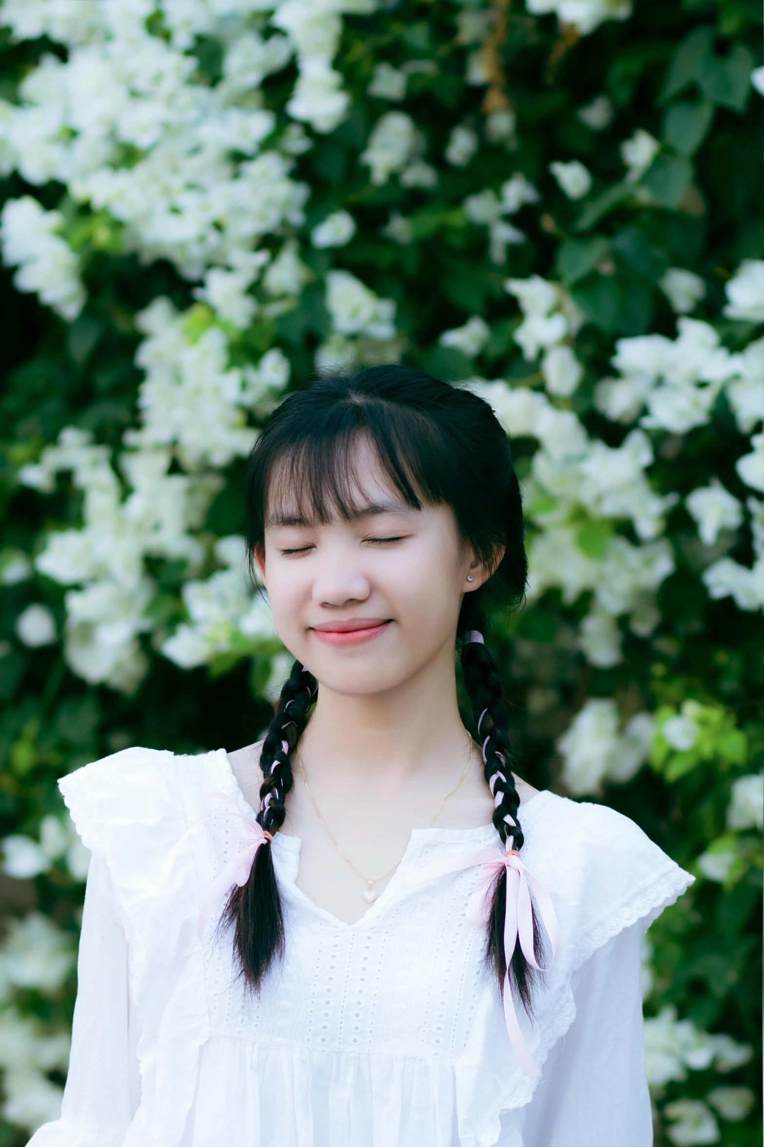 a girl in white dress looking down with flowers in background